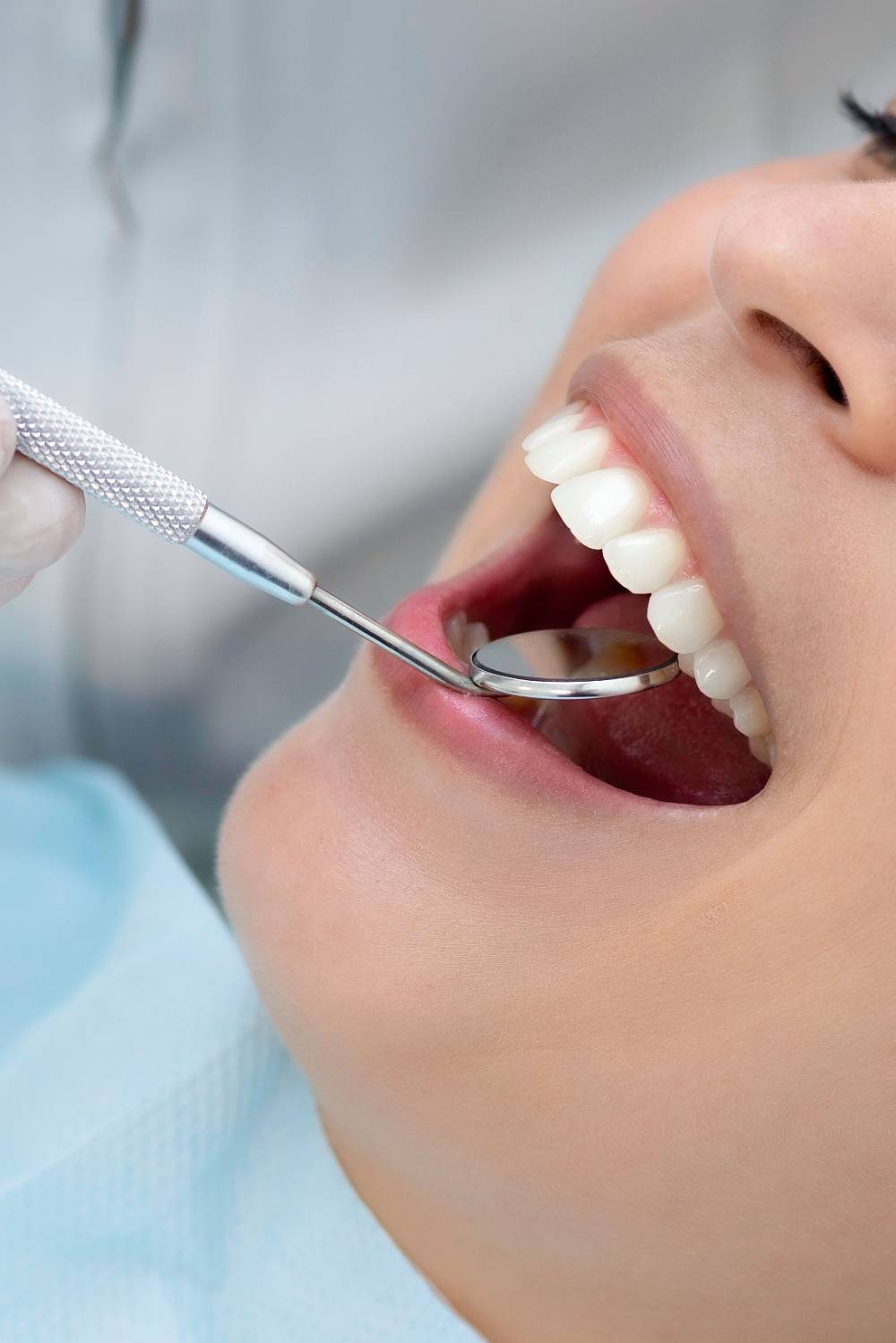 Close-up of open mouth during dental examination with metal mirror and tools inspecting teeth